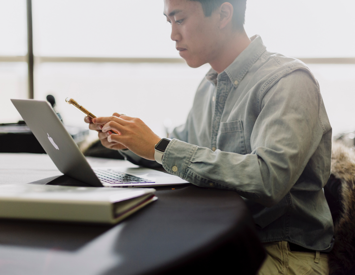 Meneer zit aan tafel achter zijn laptop met zijn telefoon in zijn hand