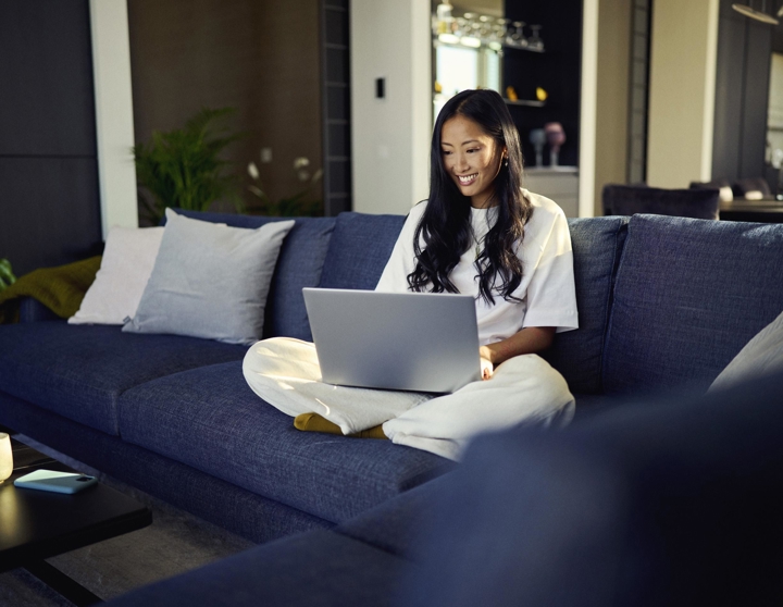 Mevrouw zit op de bank en kijkt lachend naar haar laptop