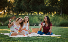 Drei Frauen sitzen auf einer Picknick Decke in einem Park und lachen zusammen