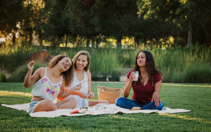 Drei Frauen sitzen auf einer Picknick Decke in einem Park und lachen zusammen