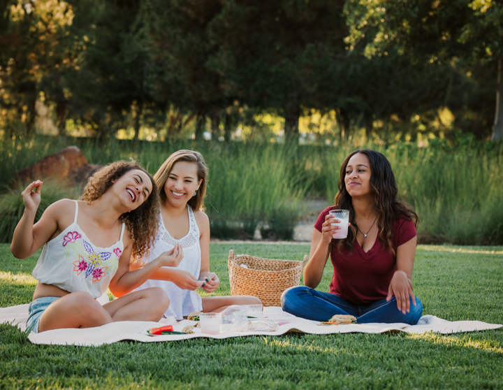 Drei Frauen sitzen auf einer Picknick Decke in einem Park und lachen zusammen