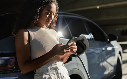 A woman leans against her car with a mobile phone in her hand