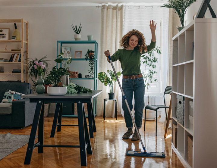 Een vrouw met rossig haar en een groen overhemd veegt en danst door het appartement