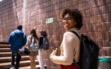 Eine junge Studentin lächelt in die Kamera während sie die Treppen zur Universität hinaufsteigt