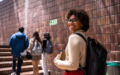 Een jonge studente lacht naar de camera terwijl ze de trap naar de universiteit beklimt