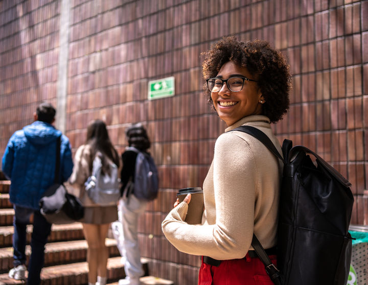 Een jonge studente lacht naar de camera terwijl ze de trap naar de universiteit beklimt
