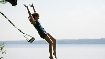 Eine junge Frau springt mit erhobenen Armen von einer schwingenden Schaukel in einen See