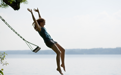 Een jonge vrouw springt met opgeheven armen van een schommel in een meer