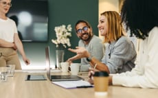 Vier junge Männer und Frauen stehen und sitzen an einem Tisch, trinken Kaffee und quatschen über ihre Finanzen und ihre Zukunft