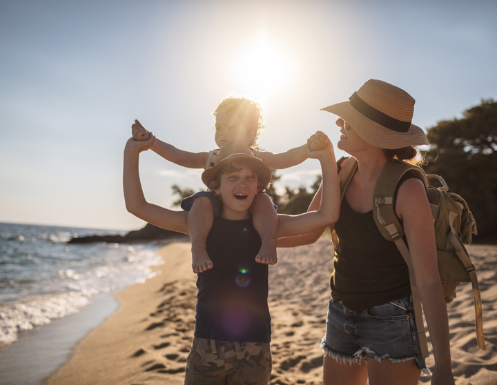 Eine Mutter und ihre zwei Kinder gehen lachend am Strand spazieren.