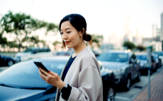 Nainen seisoo auton vieressä maksamassa pysäköintiä matkapuhelimellaan