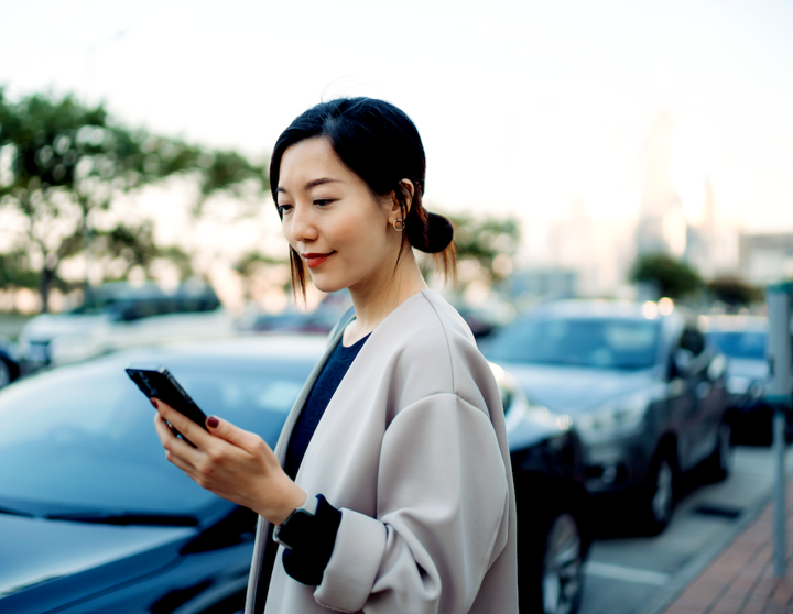 Eine Frau steht neben ihrem Auto und bezahlt mit ihrem Handy