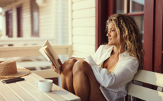 Eine blonde Frau sitzt gemütlich auf einer Bank und liest ein Finanzbuch.