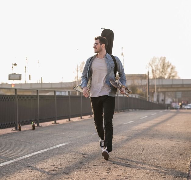Junger Mann, der mit einem Skateboard unter dem Arm durch die Stadt läuft