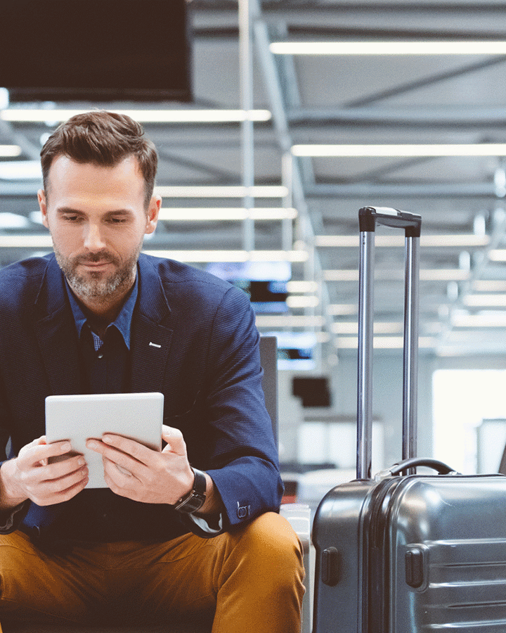 En mand sidder i en lufthavn og ser på en tablet