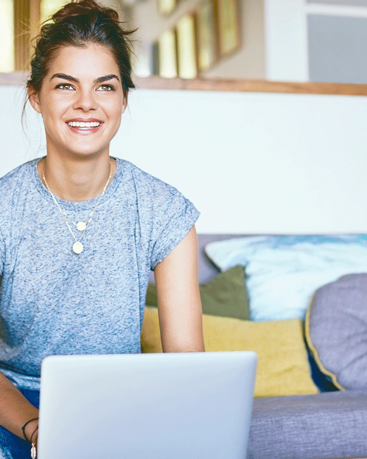 En smilende kvinde sidder ved en laptop og ser frem for sig