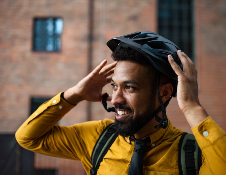 En smilende mand i gul skjorte tager sin sorte cykelhjelm af
