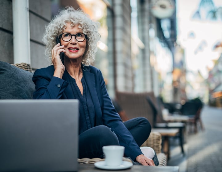 En kvinde med briller sidder og taler i smartphone på en café