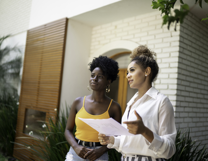 Eine brünette Frau und eine blonde Immobilienmaklerin schauen sich gemeinsam eine Immobilie an und sprechen über die Investitionsmöglichkeiten