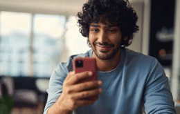 En man i blå tröja tittar på sin mobiltelefon och ler.