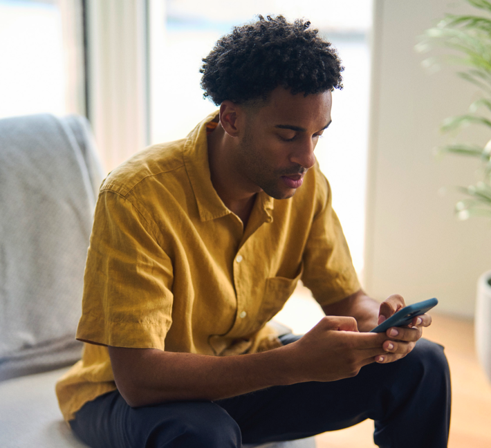 en mann som sitter i sofaen å ser på mobilen