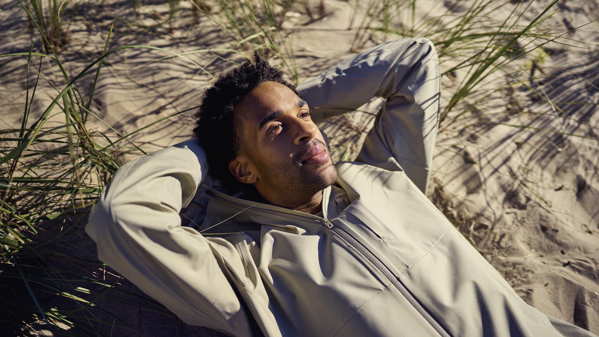 Mann som ligger i gresset på en sandstrand