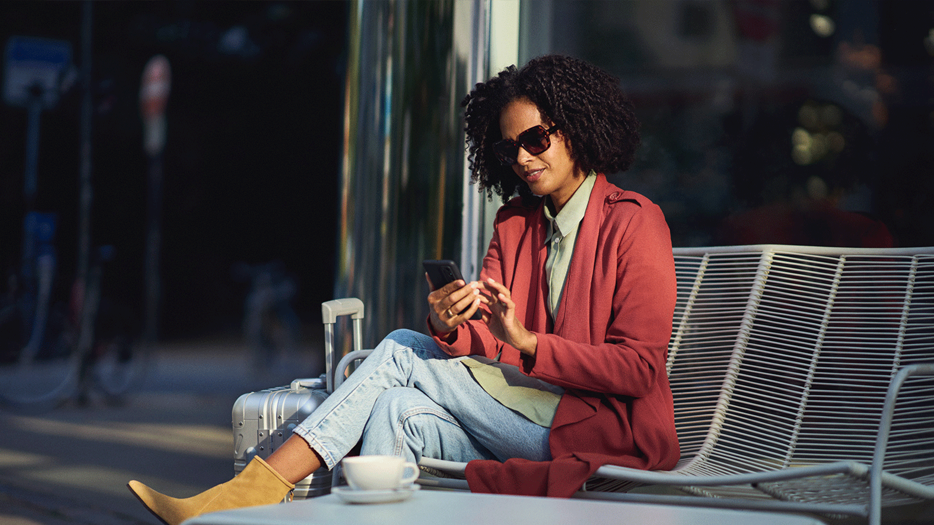 En kvinna i röd kappa och solglasögon tittar i sin mobiltelefon 