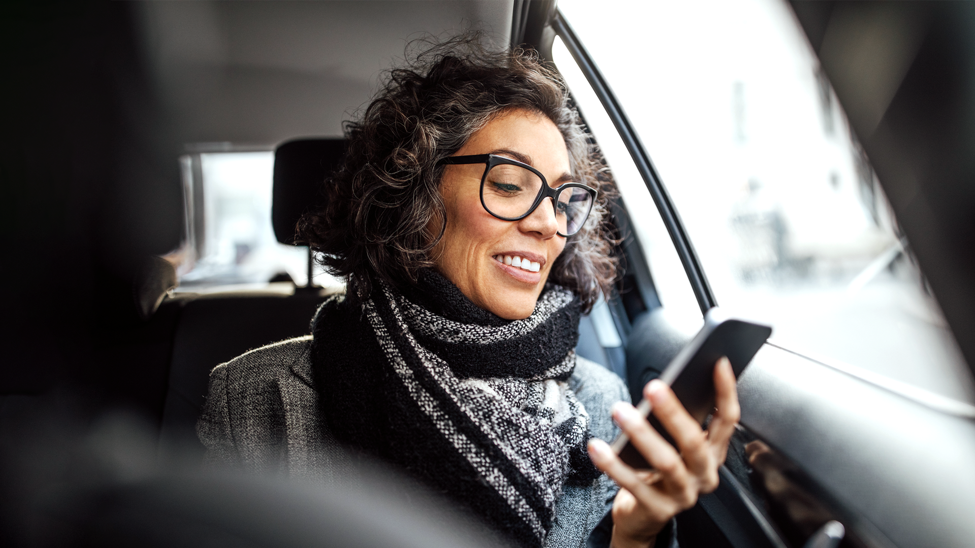 Kvinne sitter i bilen og ser på mobilen