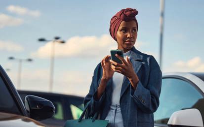 En kvinna står vid parkeringsplats med en mobil i handen