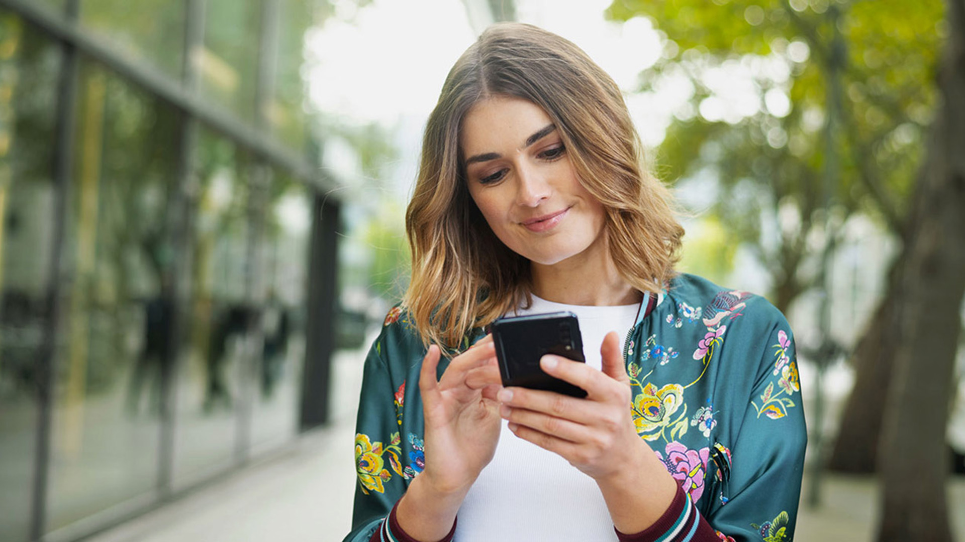 Junge, lächelnde Frau in der Stadt mit einem Smartphone in der Hand