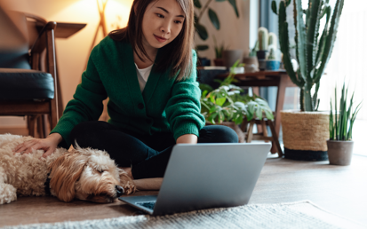 Eine junge brünette Frau sitzt mit ihrem Hund auf dem Boden und meldet auf ihrem Laptop einen Identitätdiebstahl