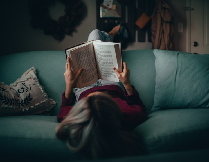 Eine Frau liegt kopfüber auf ihrem Sofa und liest in ihrem Buch.