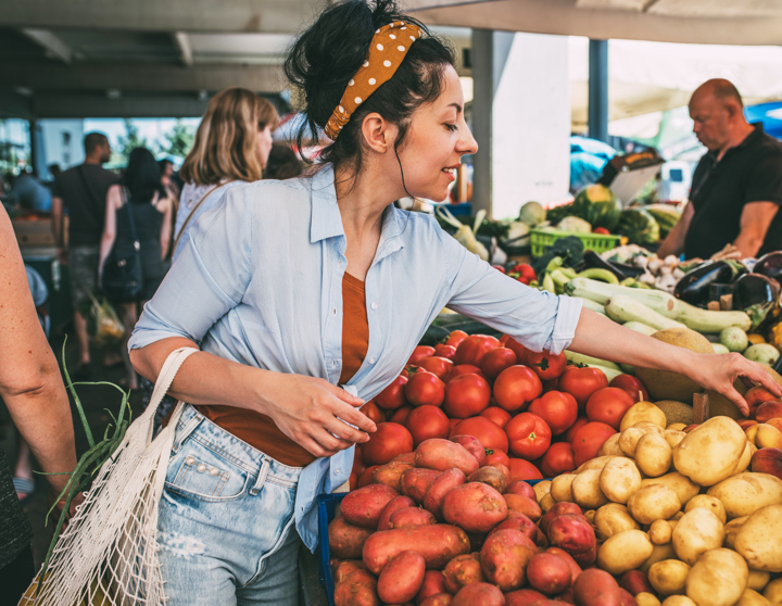 Eine brünette Frau kauft an einem Marktstand Obst und Gemüse