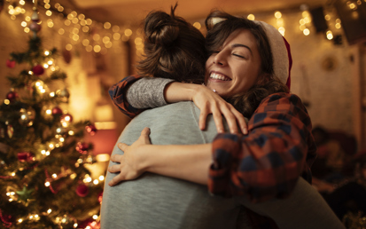 Zwei Freundinnen umarmen sich vor dem Weihnachtsbaum, nachdem sie sich ihre Geschenke übergeben haben