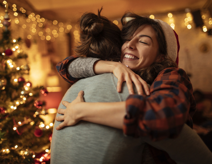 Zwei brünette Frauen umarmen sich innig in einem weihnachtlich geschmückten Raum