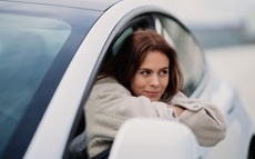 Eine junge Frau lehnt sich lächelt aus dem Fenster eines grauen Autos.