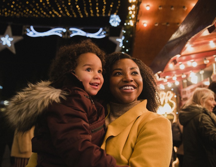 Eine brünette Frau hält ein Kind in ihren Armen und steht vor einem Weihnachtsstand