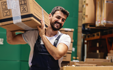 A warehouse worker lifts a box in a stocked warehouse.