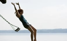 Een vrouw springt vrolijk van een schommel met de zee op de achtergrond