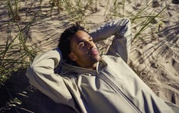 En avkopplad man ligger på en strand och blickar upp i skyn