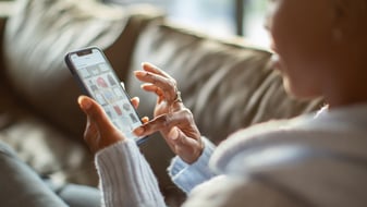 Een vrouw zit op de bank met een telefoon in haar hand