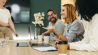 Vier junge Männer und Frauen stehen und sitzen an einem Tisch, trinken Kaffee und quatschen über ihre Finanzen und ihre Zukunft