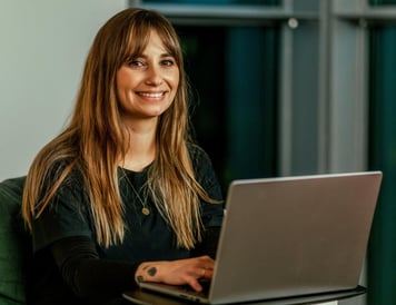 A smiling professional working on a laptop in a modern office environment.