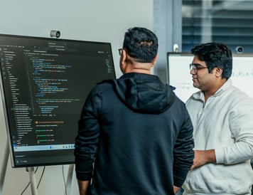 Two colleagues reviewing code on a large screen, engaged in discussion