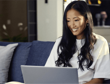 Smiling woman sitting on a couch, using a laptop for online shopping and paying in three.