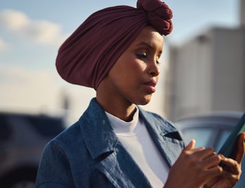 Focused woman wearing a headscarf, standing outdoors and using her smartphone for digital payments.