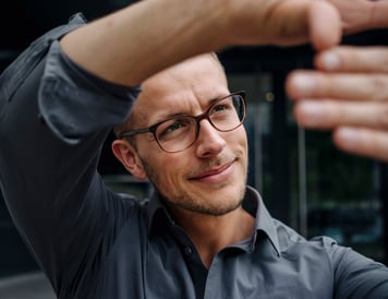 A man wearing glasses raises his hand, signaling in a focused setting.