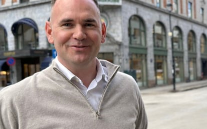 Portrett av en mann som står i en bygategate med historiske forretningsbygg i bakgrunnen