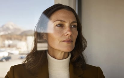 Frau, die durch ein Fenster nach draußen schaut.