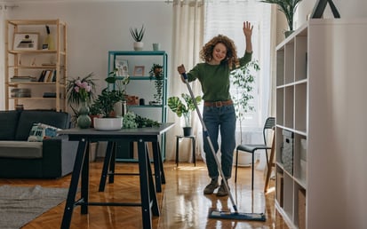 Een vrouw met rossig haar en een groen overhemd veegt en danst door het appartement